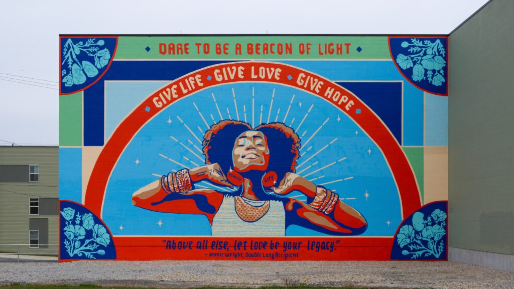 mural featuring a woman smiling with closed eyes, arms raised in a joyful pose. Words read "Dare to be a beacon of light," evoking hope and positivity.